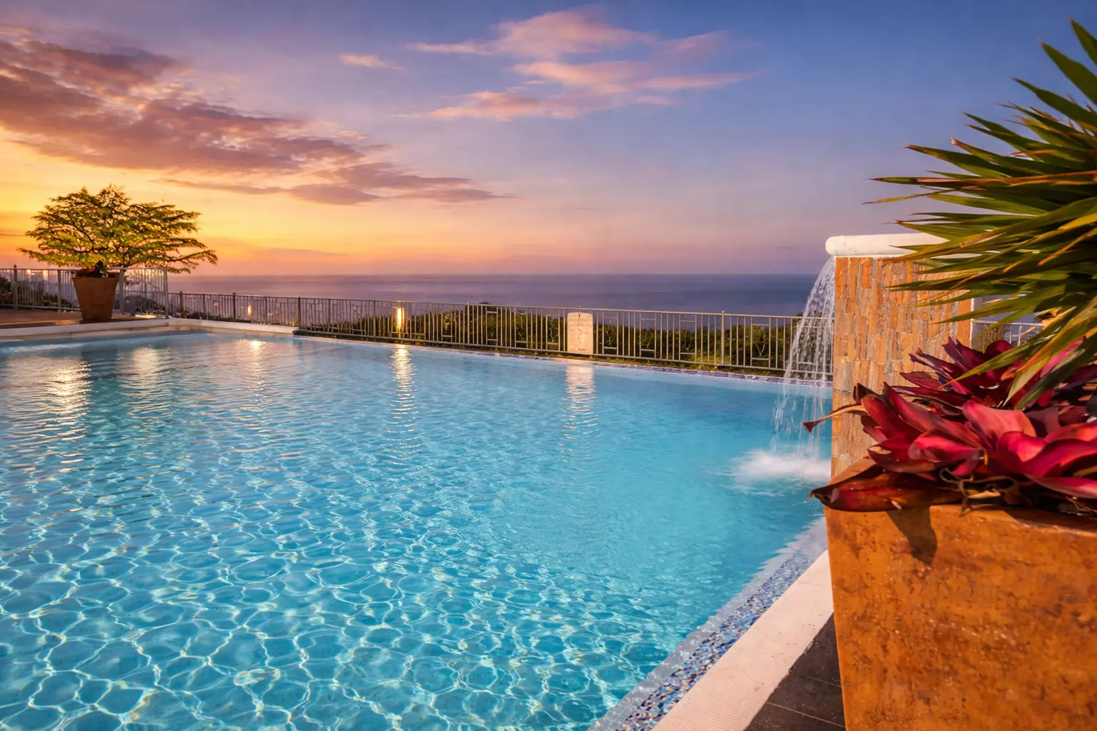 The pool at Velvet & Vine at sunset, a fountain spilling into the water with the sea and a glowing sky beyond
